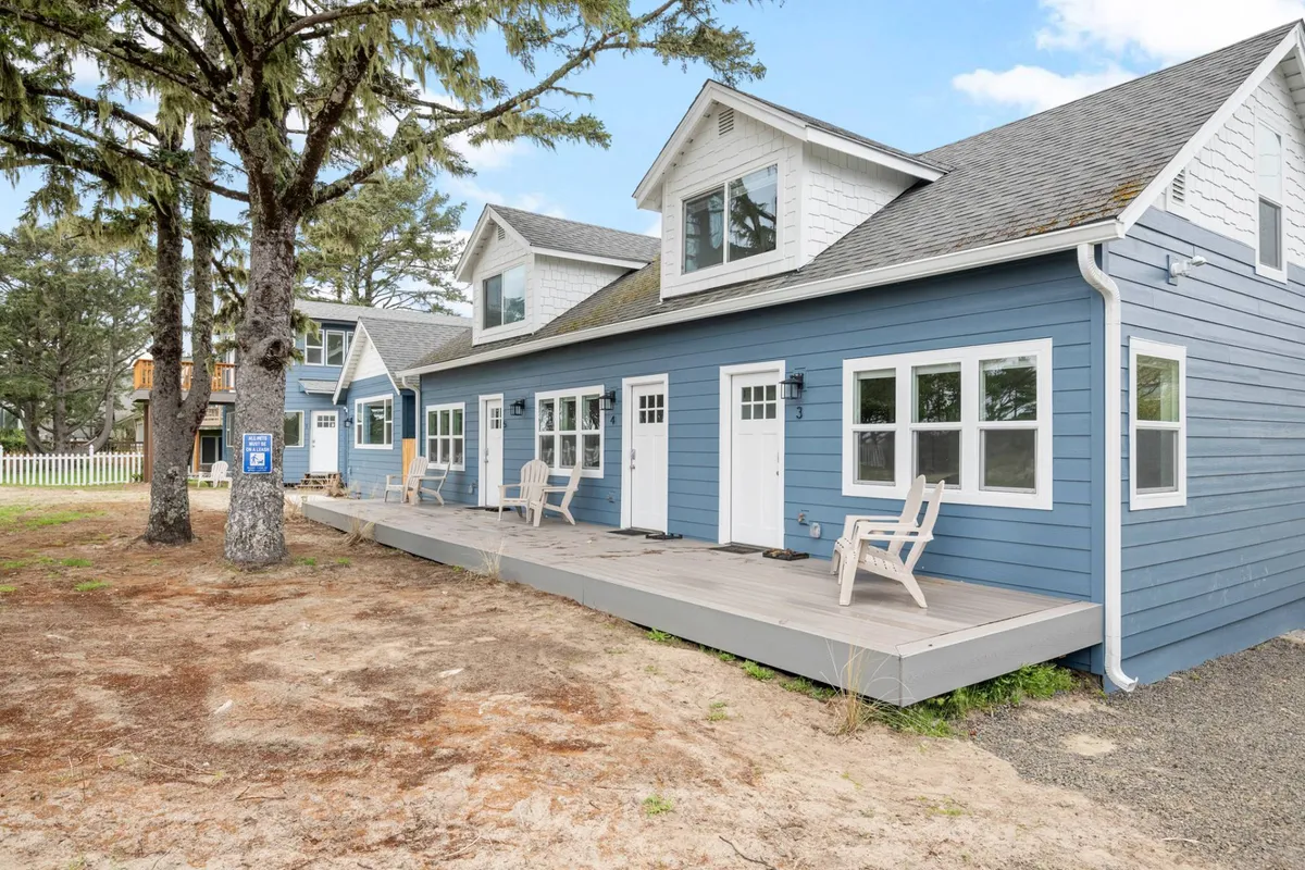 A blue exterior with white trim and windows, set amongst trees, featuring a wooden deck furnished with chairs. The setup hints at social spaces for gathering, relaxing in nature, or enjoying fresh air breaks between work sessions.