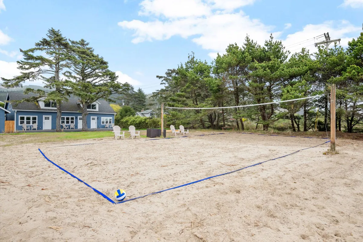 This exterior shot captures the vibrant outdoor life at the Inn, with a volleyball net, sand court, comfortable seating, and a fire pit for group gatherings. Guests are seen playing, relaxing, and enjoying the sunset, creating a dynamic sense of community.