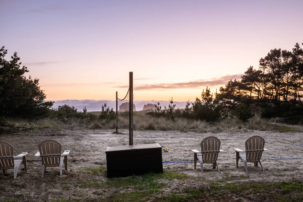 This serene social space features Adirondack chairs facing dramatic cliffs and a volleyball net set up in the sand, inviting guests and their pets to relax, play, and soak up sunsets by the sea.