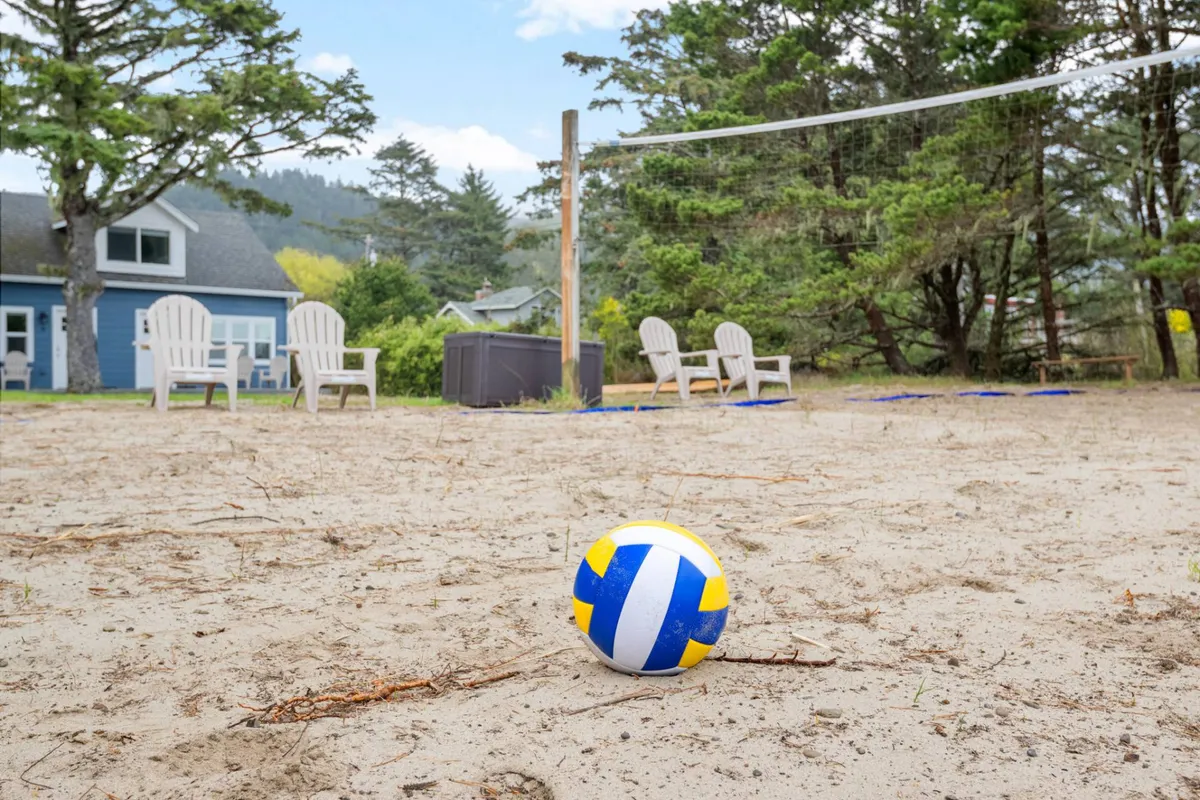 A sandy volleyball court sits next to several Adirondack chairs, inviting guests to relax and socialize after a friendly match. The setting is playful yet relaxed, with people seen enjoying both the sport and downtime in the shared outdoor space.