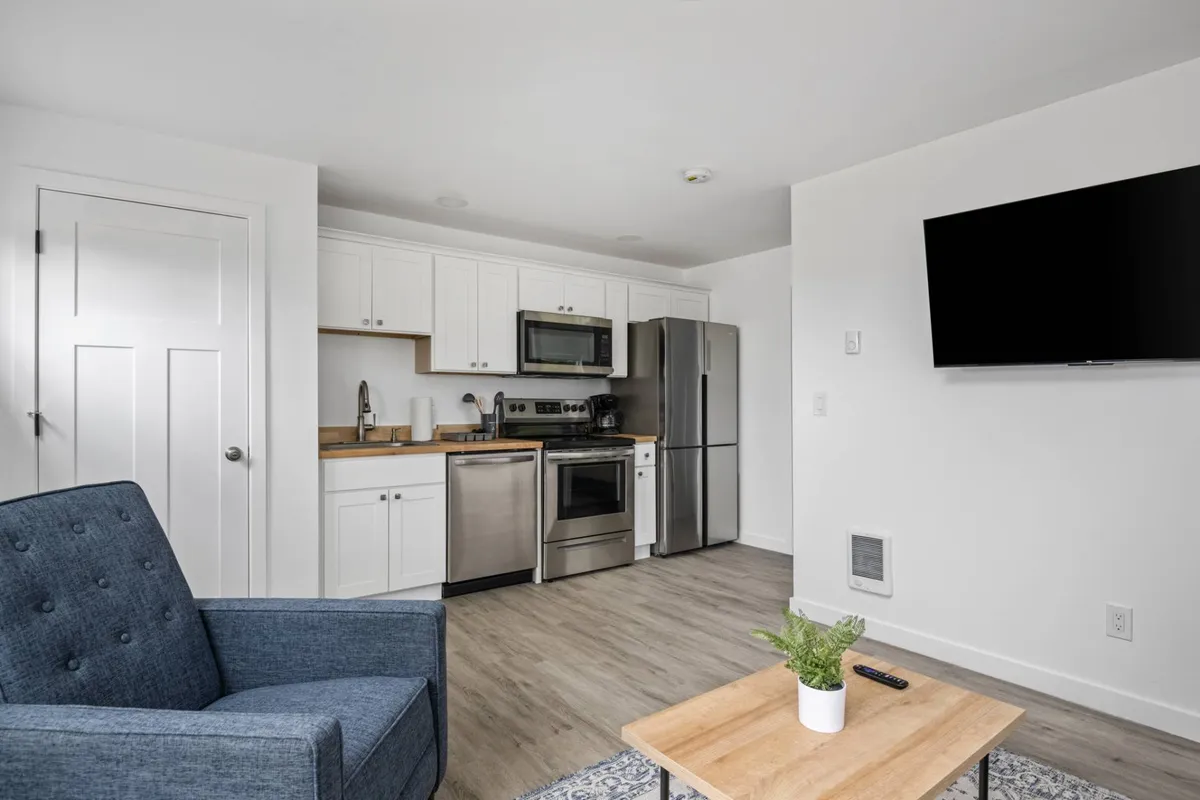 A view that bridges the kitchen and dining area, highlighting a wooden dining table, blue accent chair, and kitchen appliances. The décor is contemporary and comfortable, with an inviting atmosphere suitable for shared meals or casual relaxation.