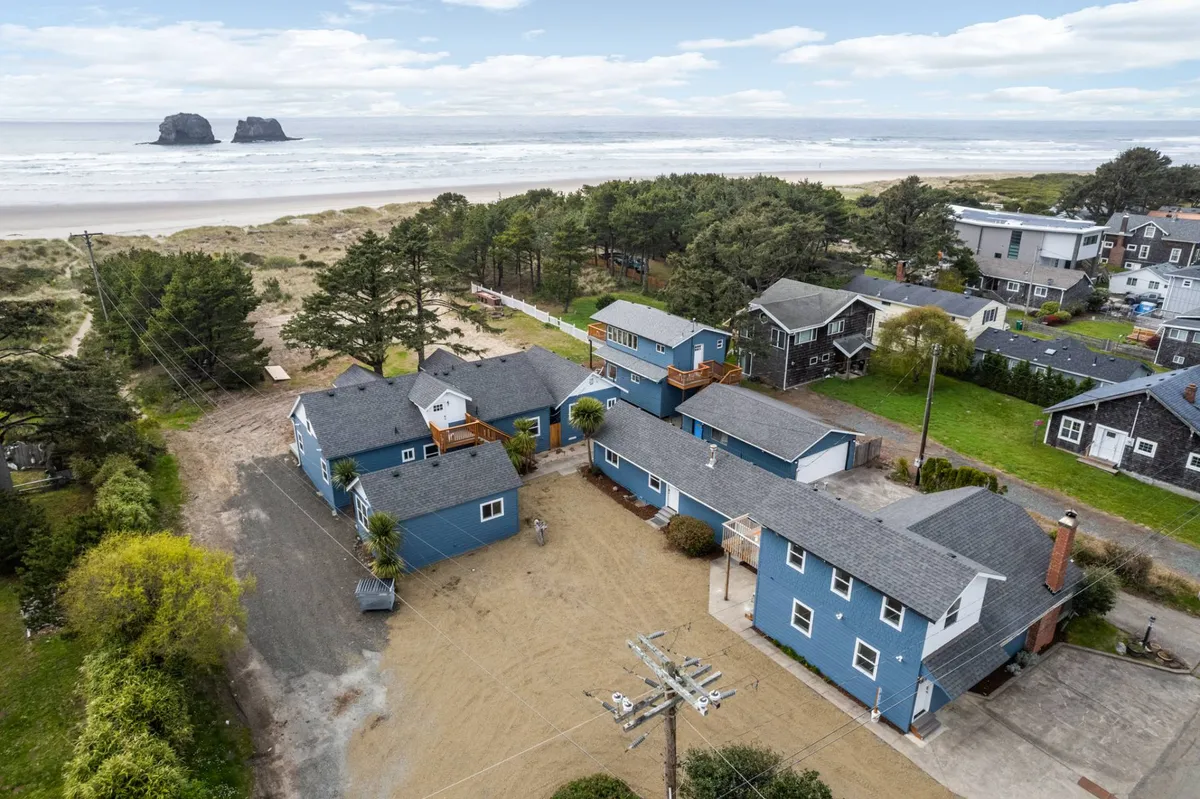 A scenic shot featuring blue beach houses, lush trees, ocean views, and distant rock formations. People are seen enjoying various outdoor activities such as barbecues and nature walks, conveying a cheerful and relaxed atmosphere.