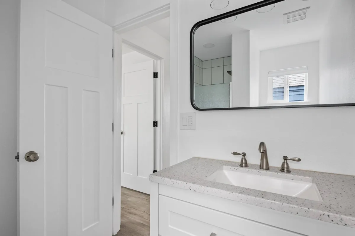 A bright, fresh bathroom vanity scene with a sleek sink, a large mirror, and a glimpse of the entryway. The area is well-lit and uncluttered, emphasizing ease of use and comfort for daily routines.
