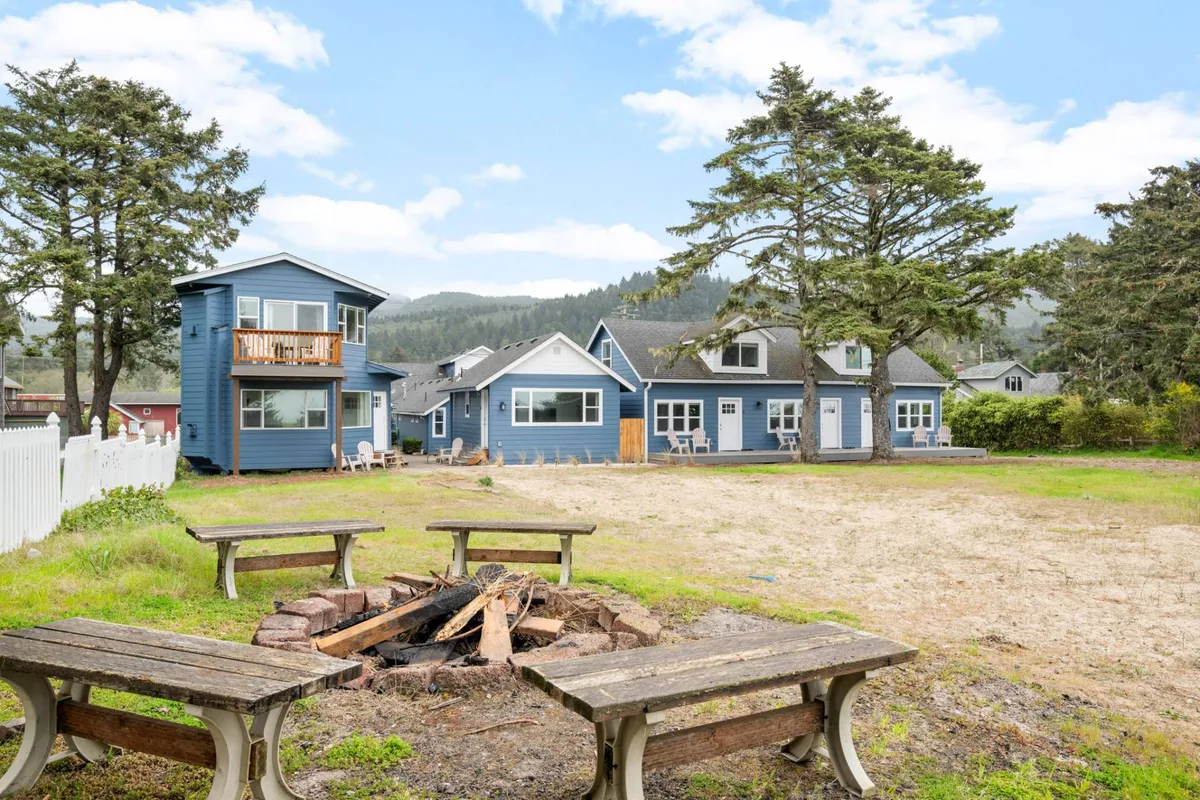 This image features the Ocean Rogue Inn's inviting fire pit encircled by blue cottages and large trees. Adirondack chairs are arranged around the fire, setting the scene for cozy campfire gatherings under the stars. The backdrop of the blue buildings and the natural setting highlight the sense of community and outdoor enjoyment.
