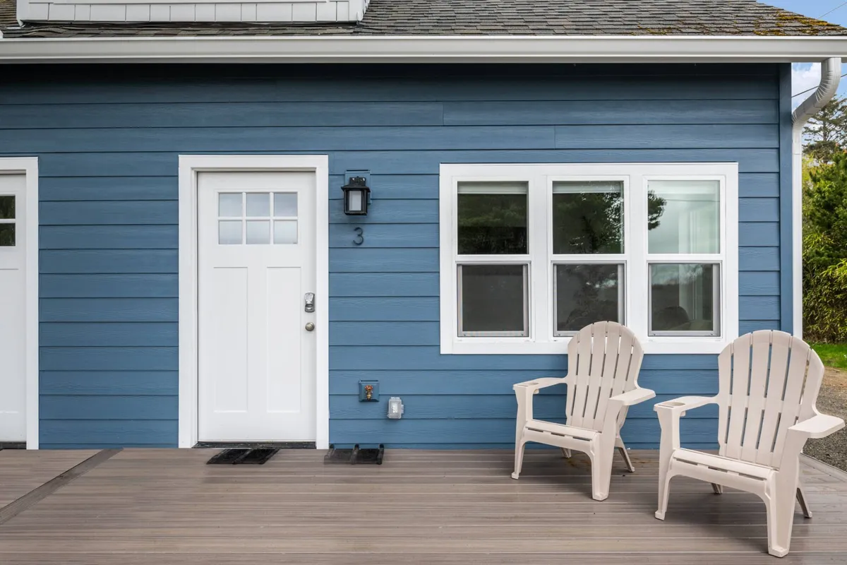 A cozy blue building with white trim and Adirondack chairs on a porch overlooks the shoreline. The inviting porch space is ideal for relaxing, enjoying the sea air, or taking a break from work, and the early morning or evening light adds to the calm, peaceful mood.