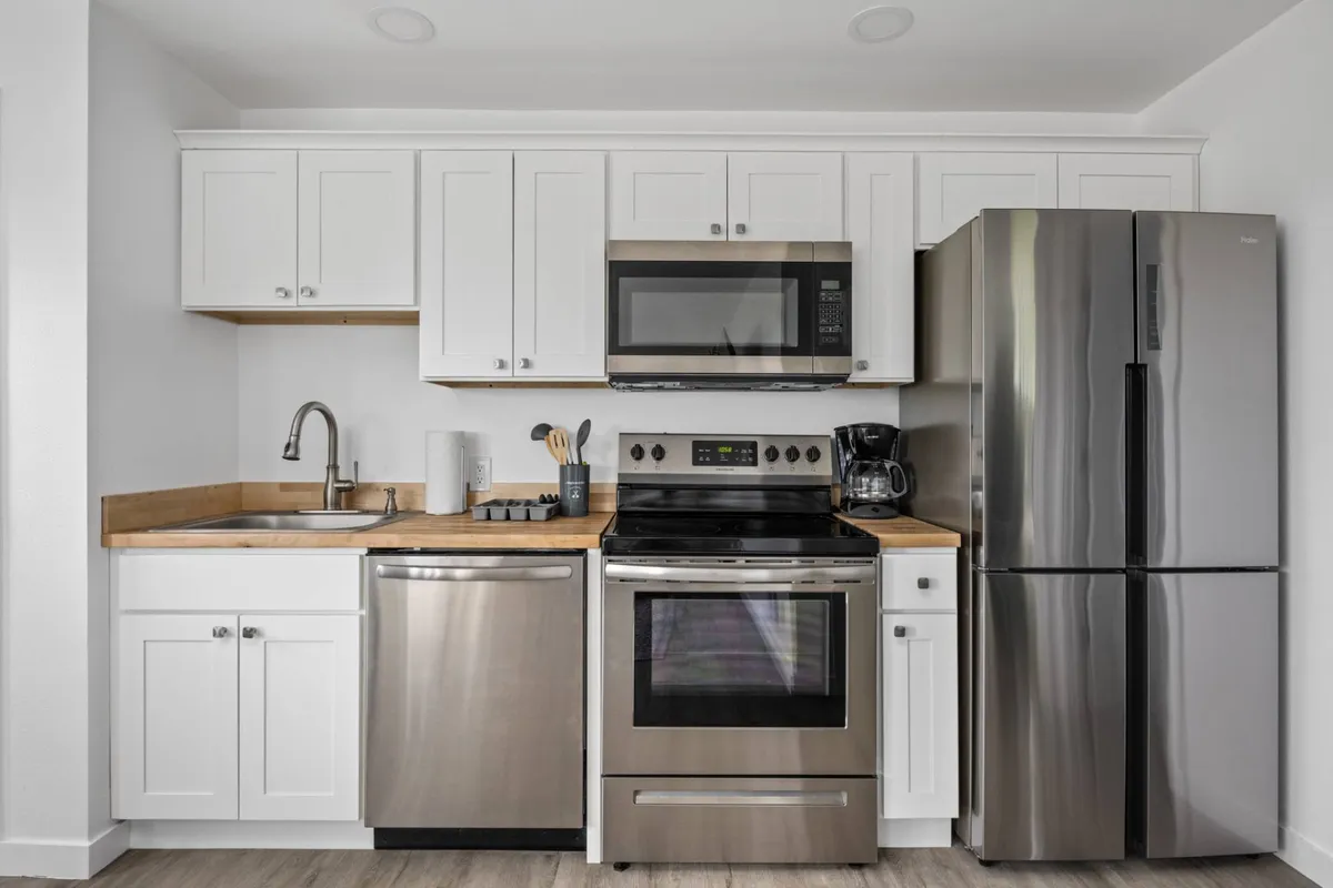 A bright, modern kitchen area with stainless steel appliances, a wooden countertop, and white cabinetry. The space is functional yet stylish, with natural sunlight enhancing the inviting mood. The open layout makes it ideal for cooking, entertaining, or simply enjoying a quiet moment.